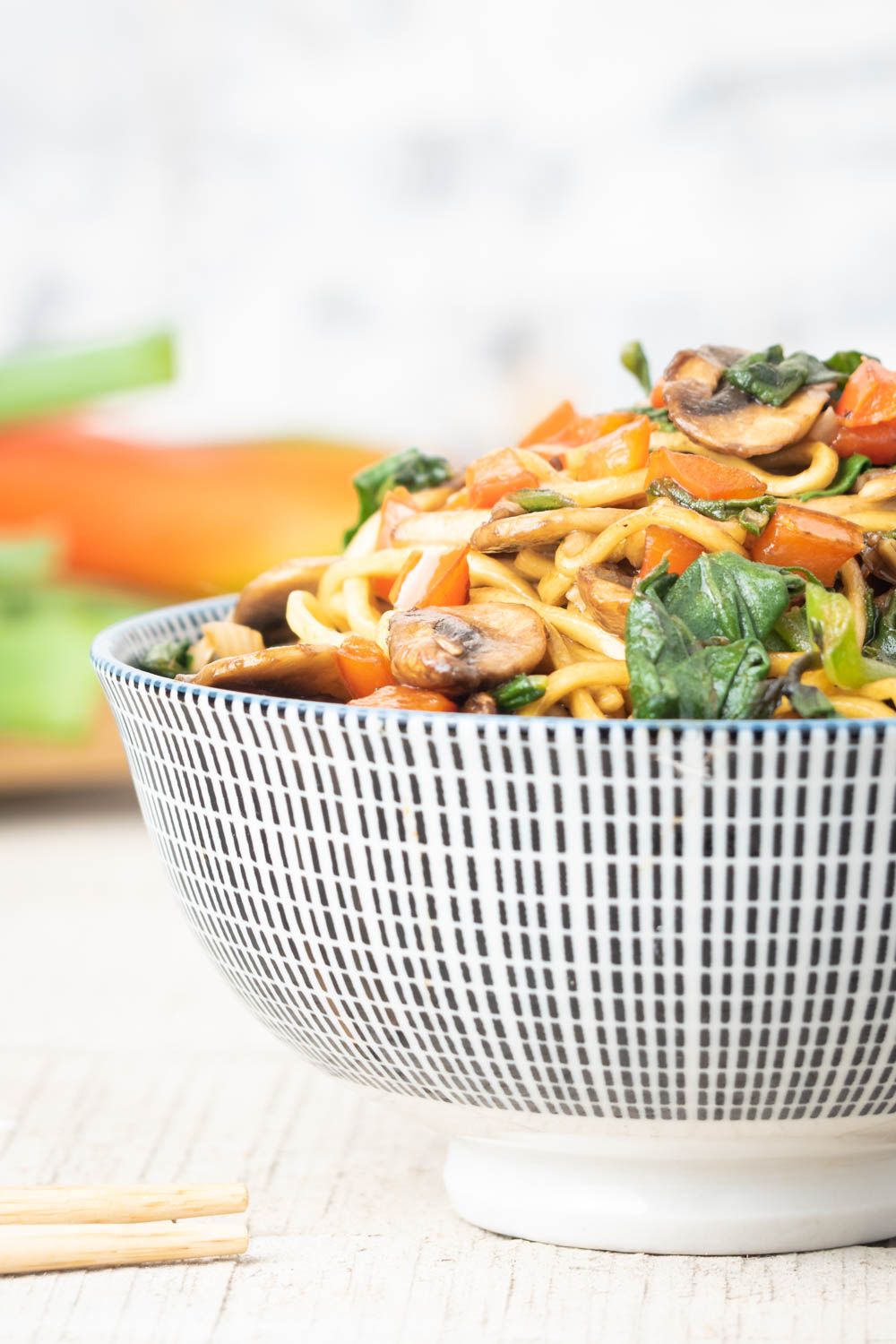 Spinach lo mein with mushrooms in a white and blue bowl.