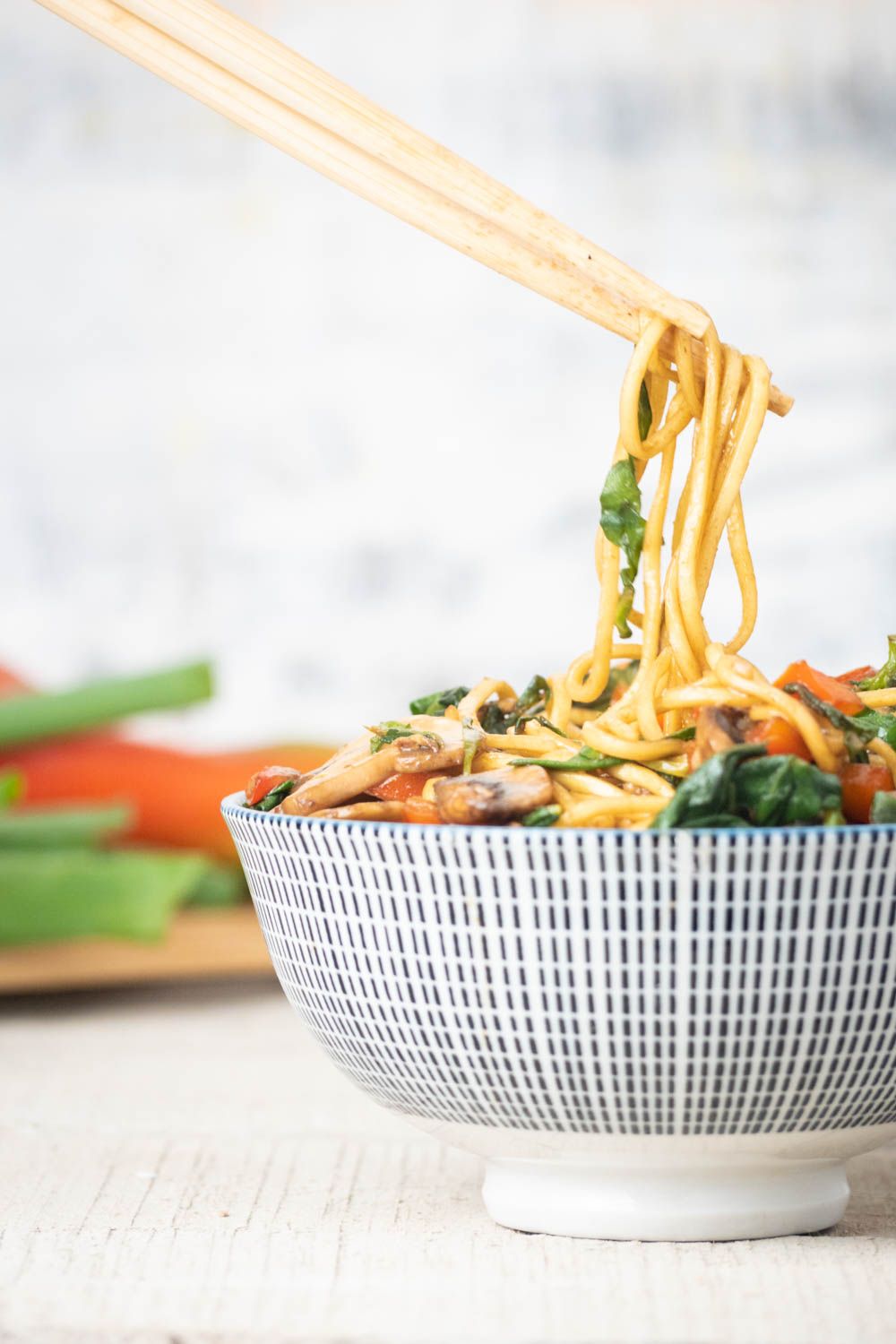 Veggie lo mein with spinach and mushrooms in a bowl with chopsticks.