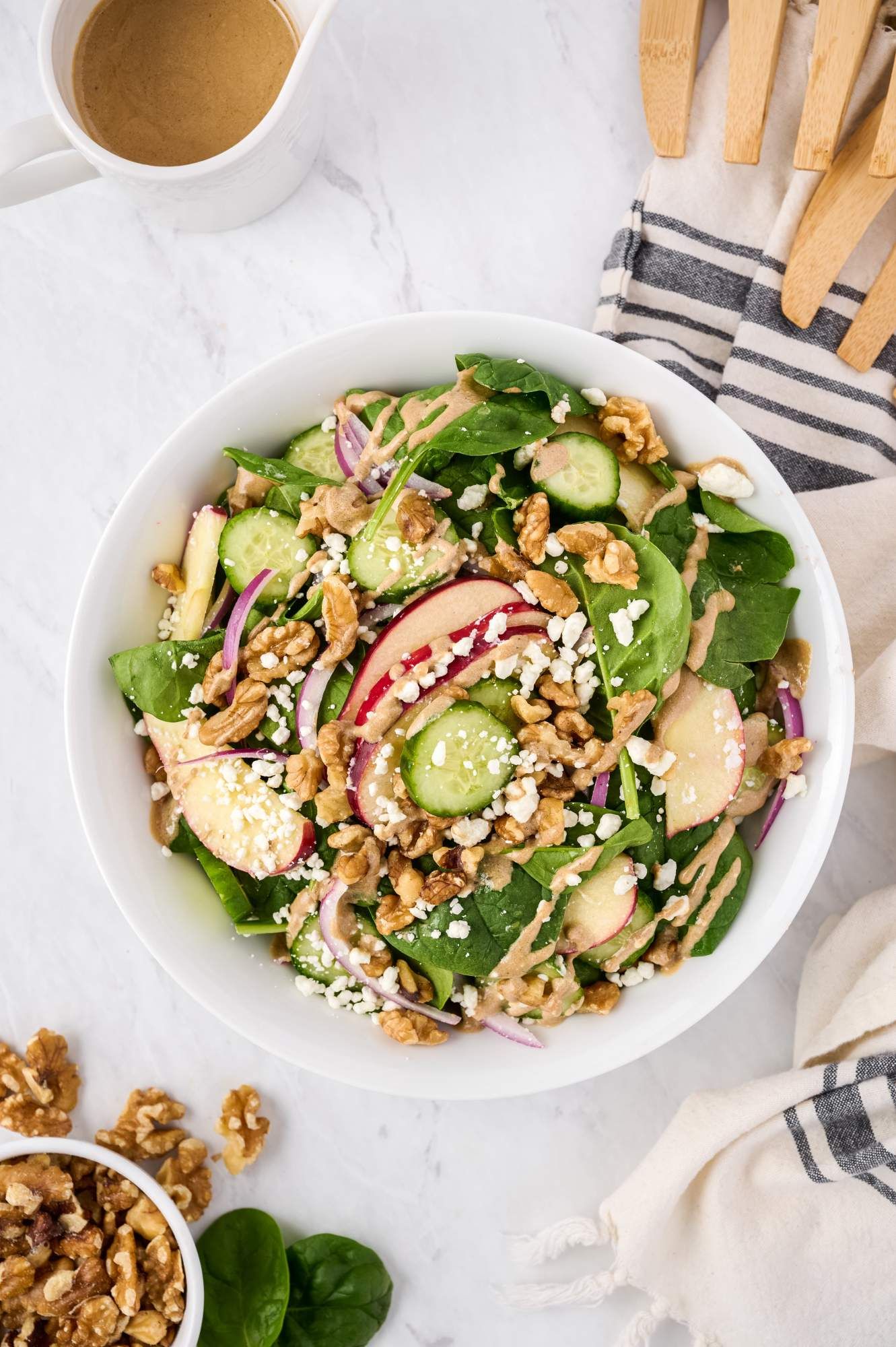 Apple and spinach salad with red onions, cucumbers, and goat cheese in a bowl with walnuts and balsamic dressing on the side.