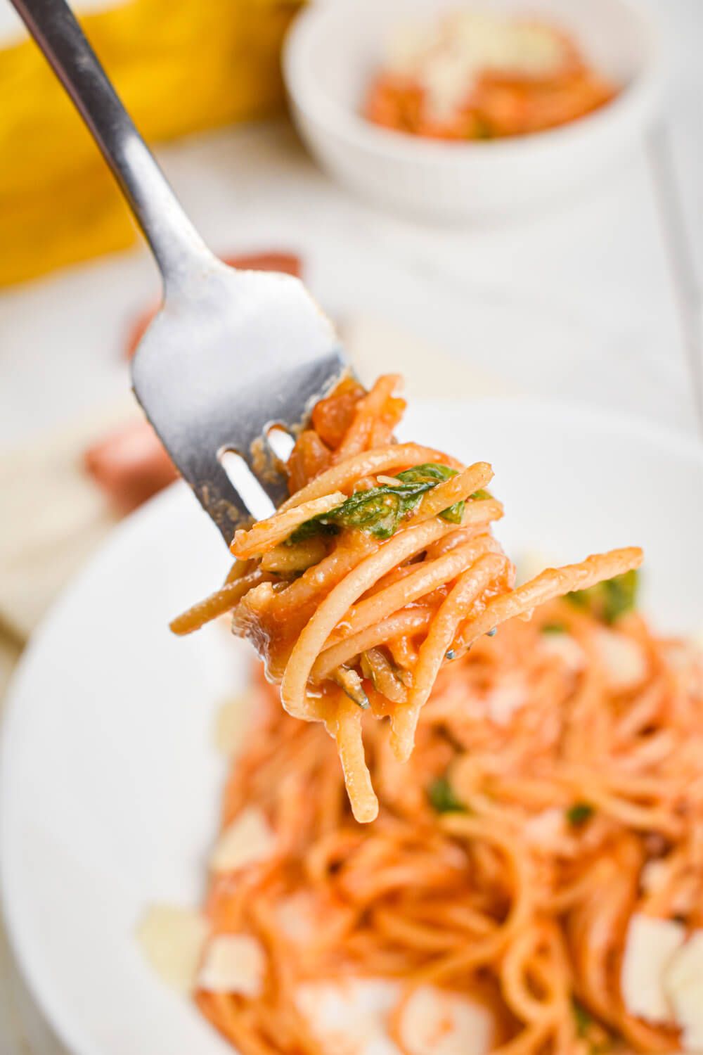 One Pot Pasta with spinach and tomatoes twirled around a fork with Parmesan cheese.