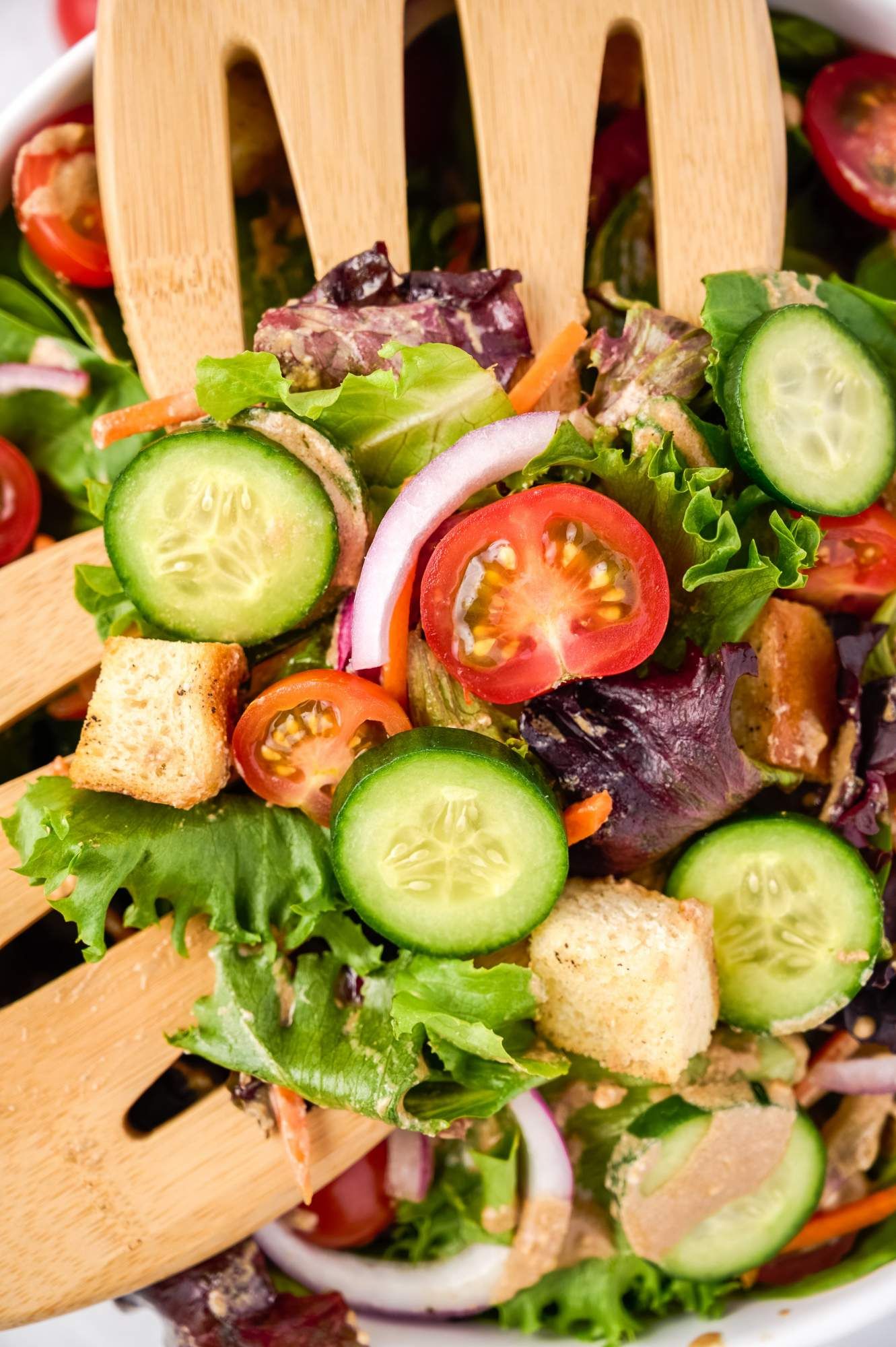 Balsamic spring mix salad with cucumbers, tomatoes, onions, and carrots being tossed in a bowl.