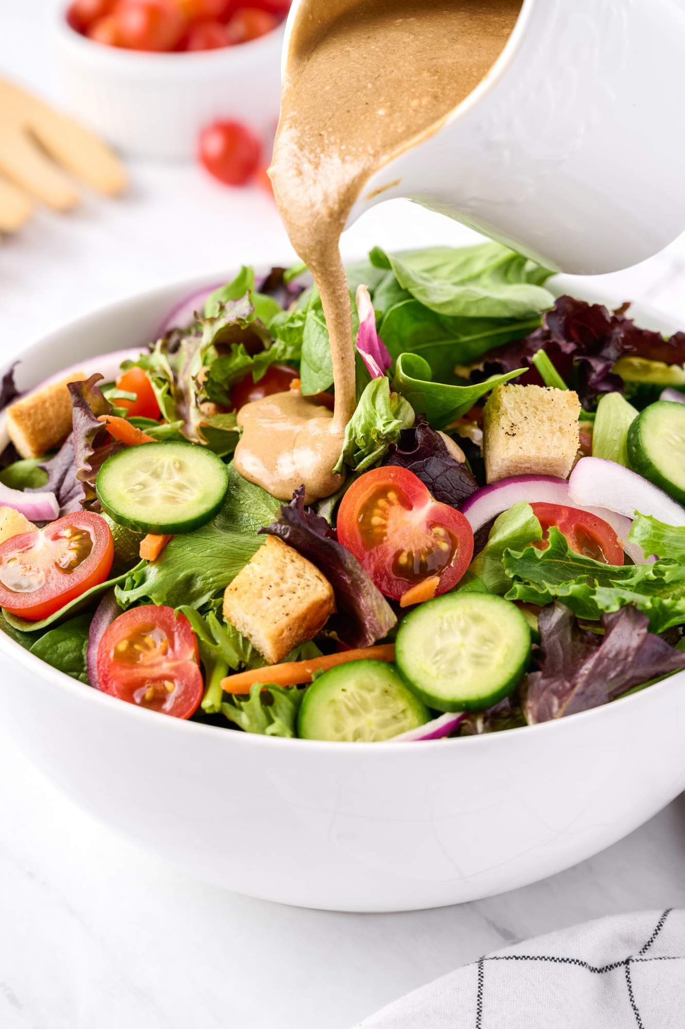 Salad made with spring mix, tomatoes, cucumbers, red onions, and carrots in a balsamic vinegar dressing in a bowl.