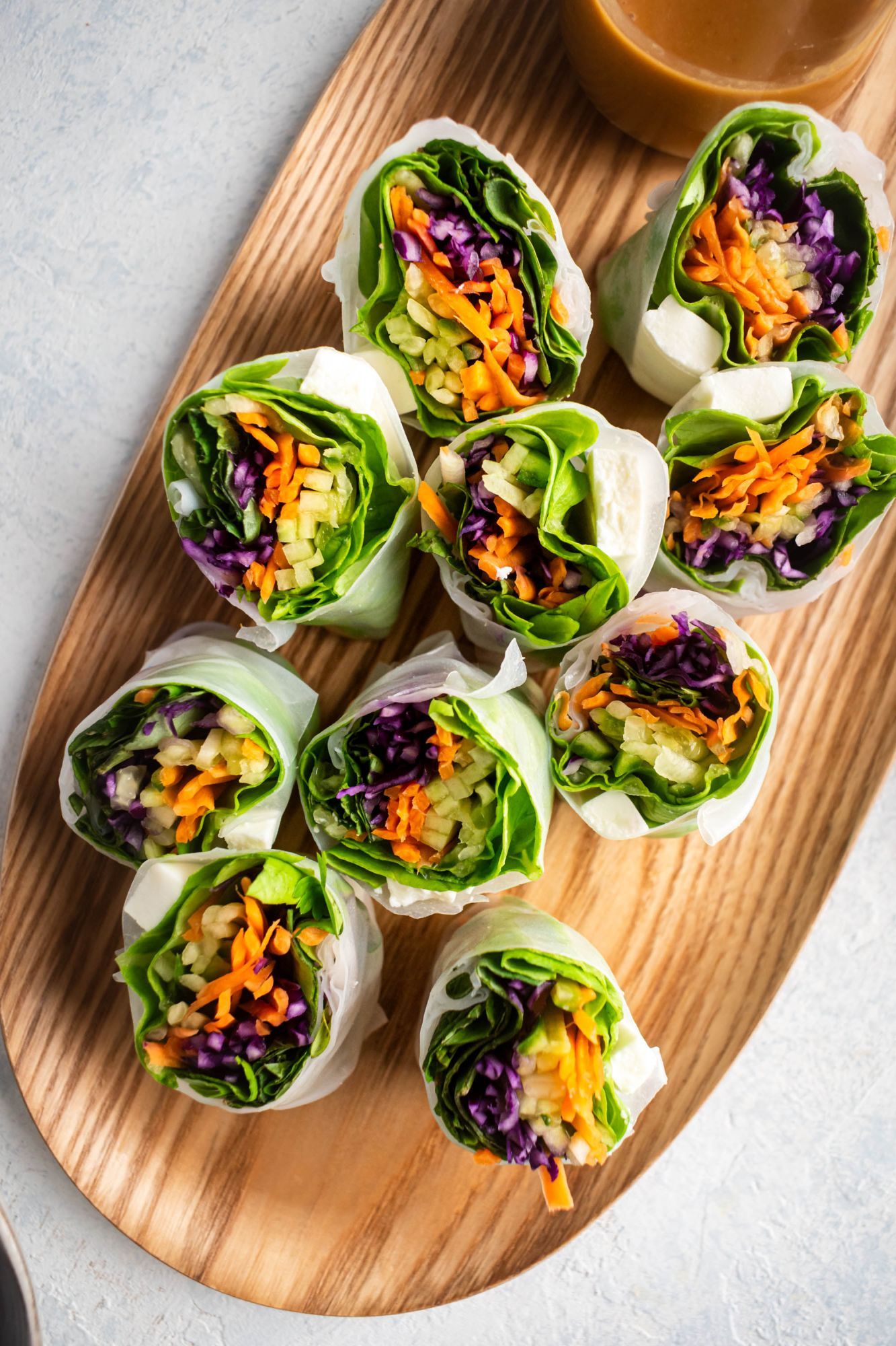 Tofu spring rolls on a wooden tray with carrots, lettuce, cabbage and cucumbers wit peanut sauce.