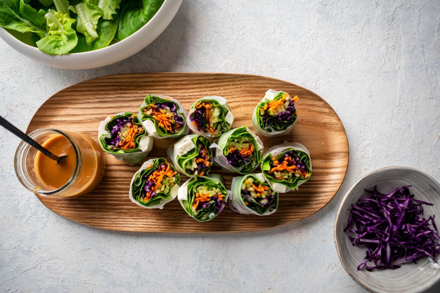 Wooden board with freshly cut spring rolls packed with vegetables and peanut sauce.