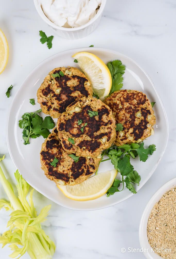 Tuna burgers with browned edges on a plate with celery, lemon slices, and fresh cilantro.