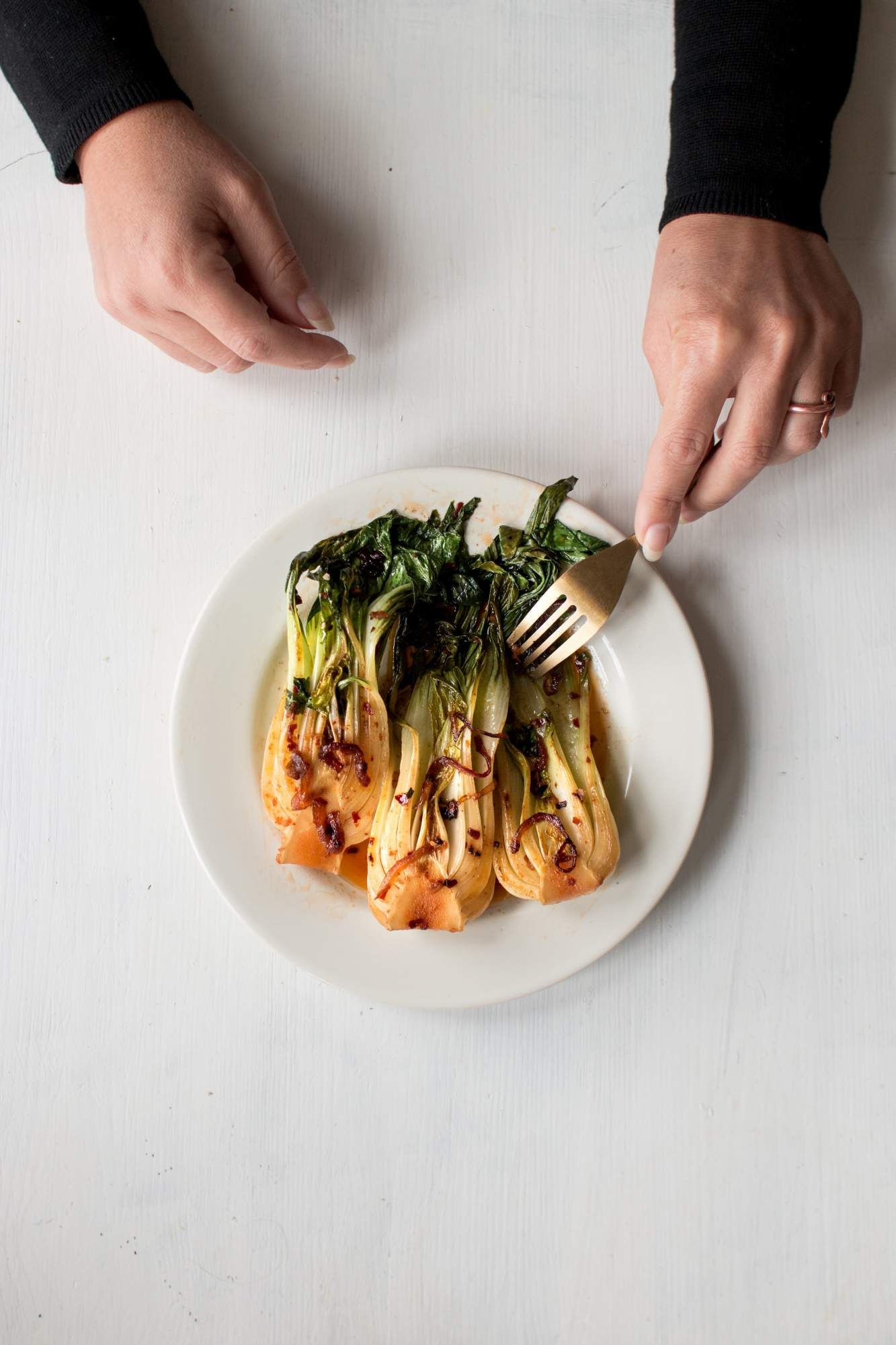 Stir fried baby bok choy on a plate with onions, chili paste, and sesame seeds. 