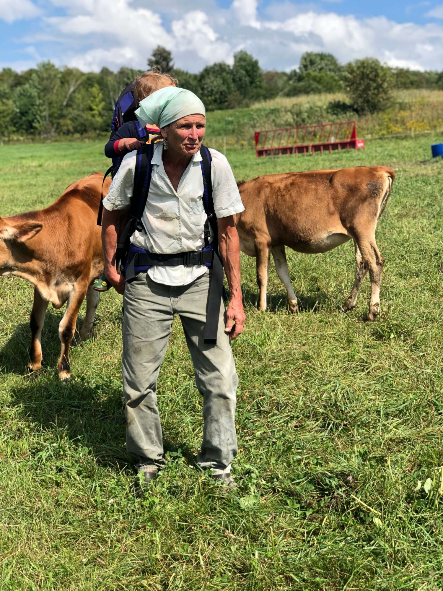 Farmer carrying a baby on her back in a field.