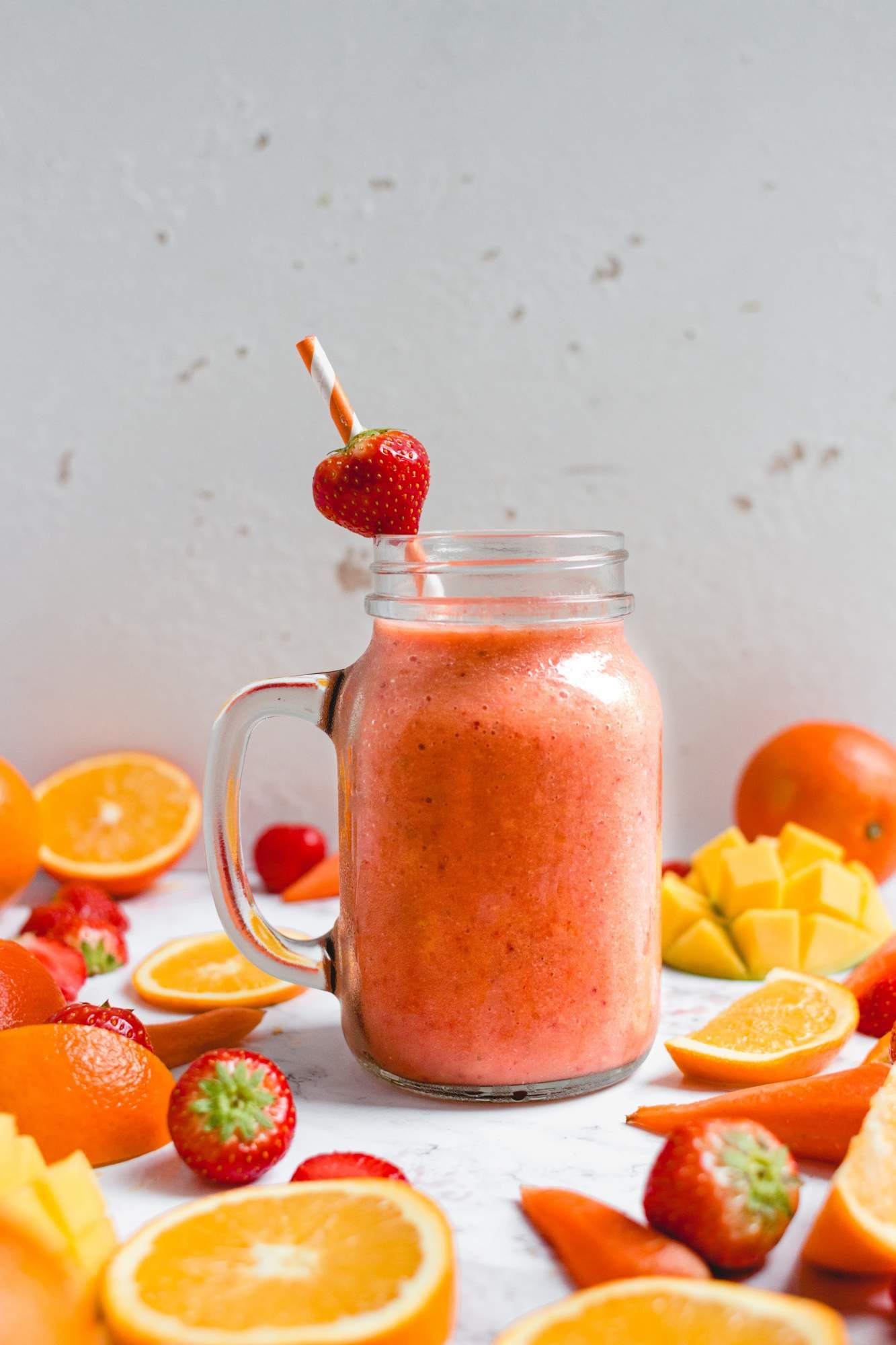 Strawberry, mango, and carrot smoothie in a glass jar with a straw and a fresh strawberry slice.