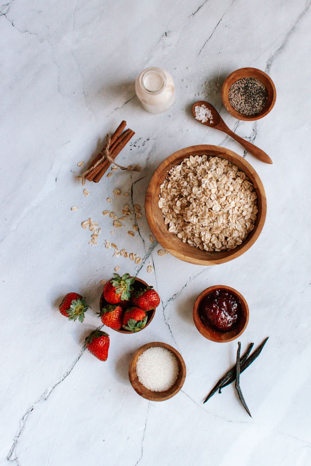 Ingredients for strawberry overnight oatmeal including rolled oats, strawberry  jam, strawberries, and cinnamon.