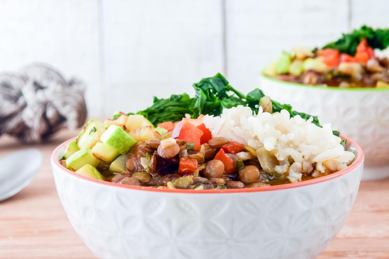 Lentil soup with Mexcian flavors in bowl with shredded cheese, cilantro, lentils. spinach, zucchini, and tomatoes in a white bowl.