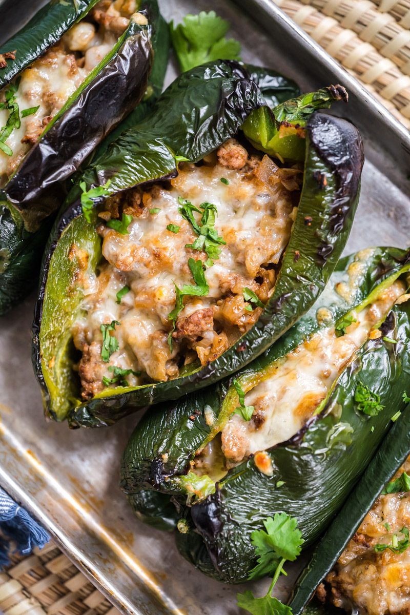 Poblano peppers stuffed with ground turkey, cauliflower, and cheese on a baking sheet.