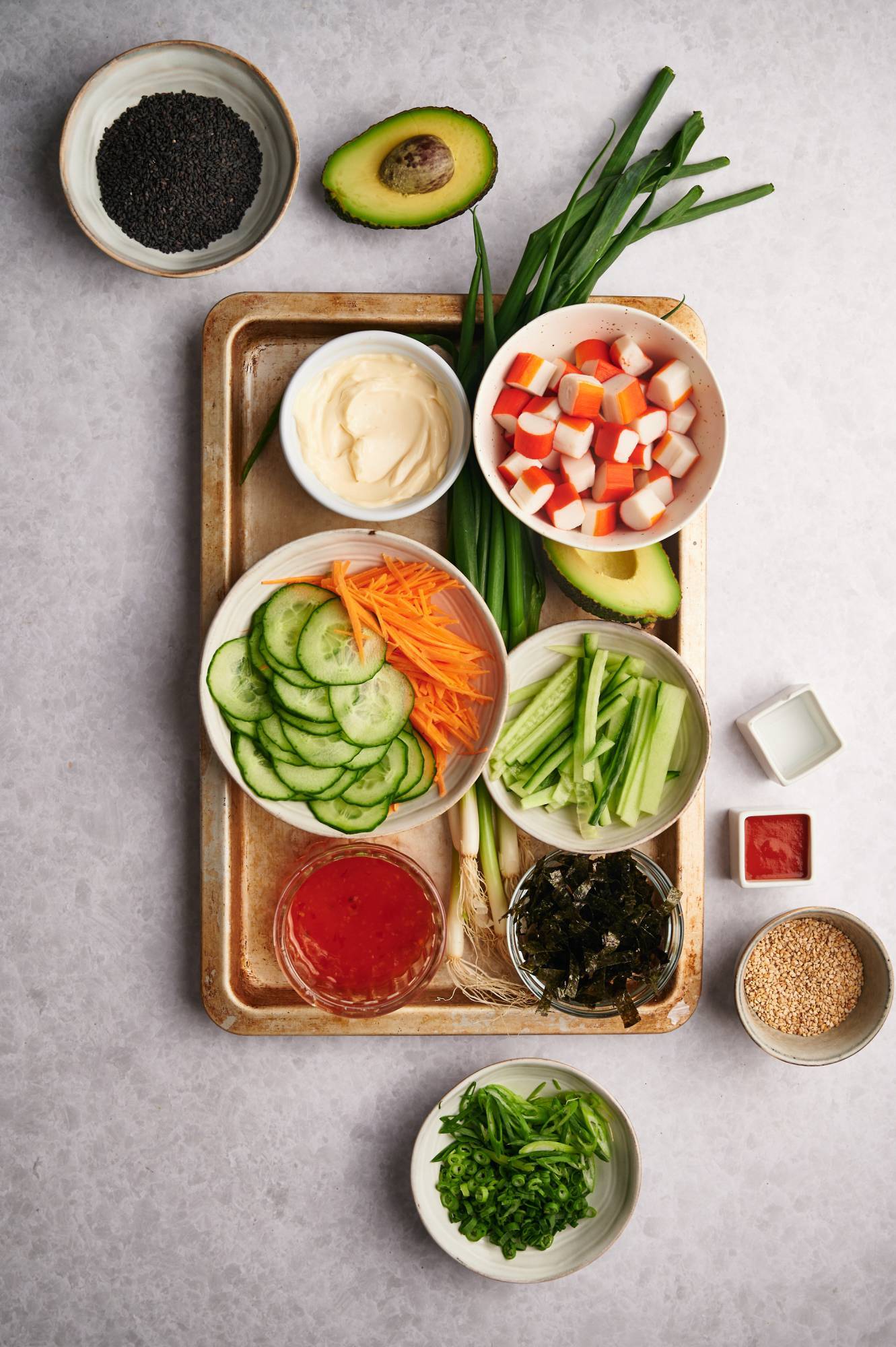 Ingredients for a sushi bowl including sushi rice, crab, seaweed, avocado, carrots, cucumbers, and green onions.