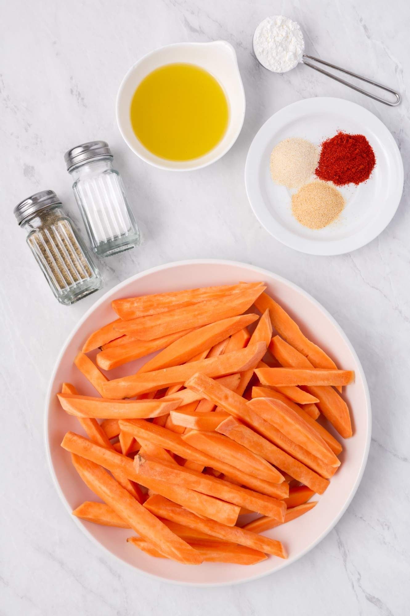 Ingredients for sweet potato fries including sliced sweet potatoes, olive oil, garlic powder, paprika, onion powder, and cornstarch.