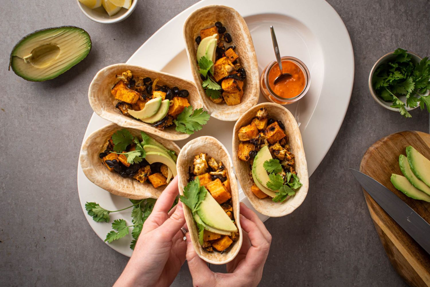 Roasted sweet potato tacos with black beans and cauliflower in taco seasoning served in tortillas with avocado and cilantro.