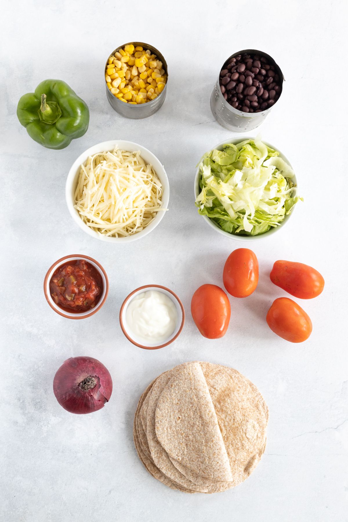 Ingredients to make taco cups including beans, corn, cheese, bell peppers, tomatoes, and tortillas.