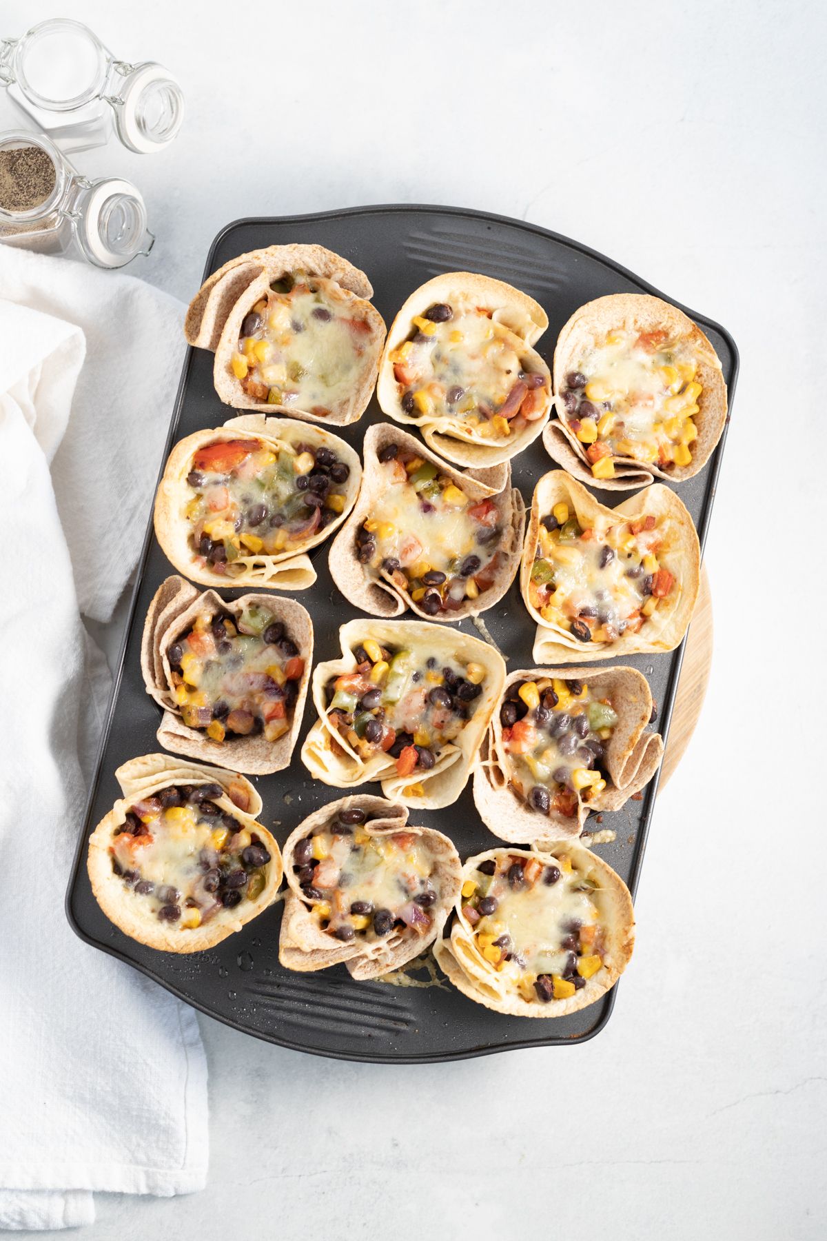 Muffin tin filled with taco cups filled with bell peppers, red onions, corn, black beans, and melted cheese.