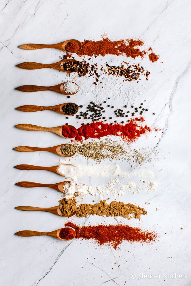 Taco spice blend ingredients on wooden spoons and a marble background.