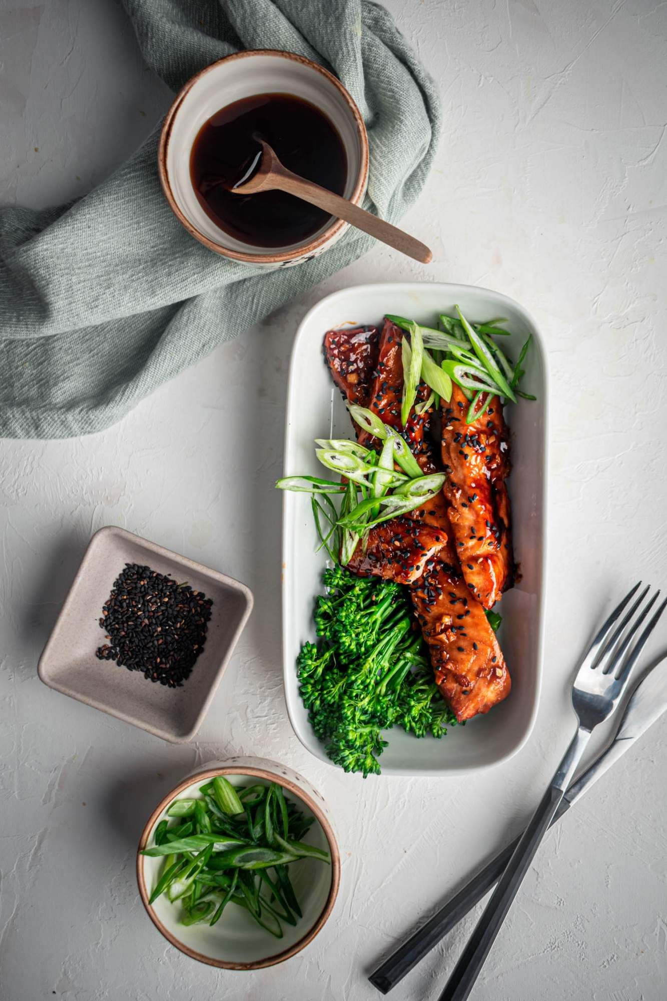 Baked salmon in teriyaki sauce with broccoli and green onions on a plate with soy sauce on the side.