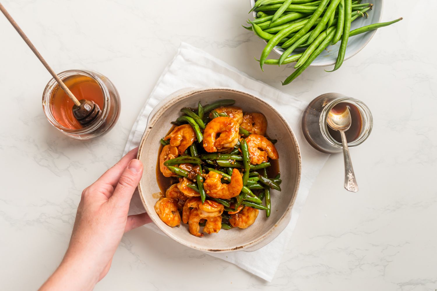 Shrimp and green bean stir fry with teriyaki sauce on a bowl with honey and green beans on the side.