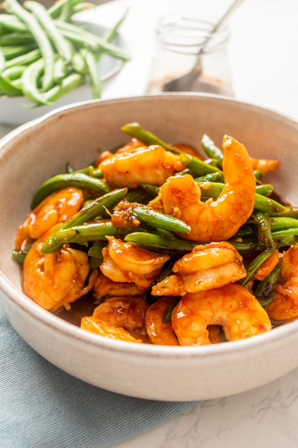 Shrimp teriyaki with green beans served in a bowl with a blue napkin.