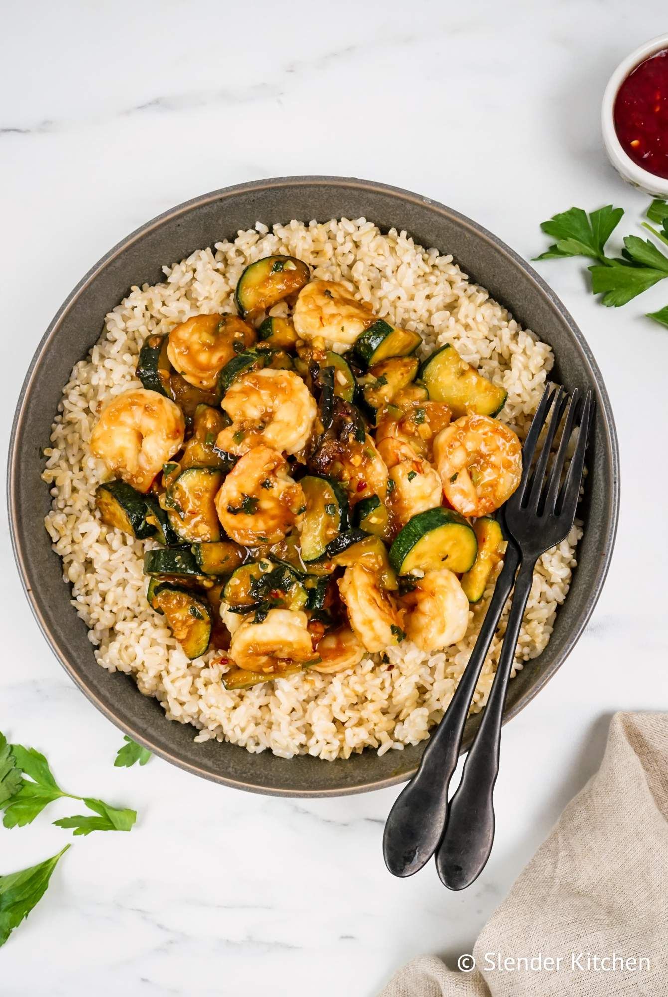 Thai shrimp stir fry with fresh basil, zucchini, and brown rice with chili sauce on the side.