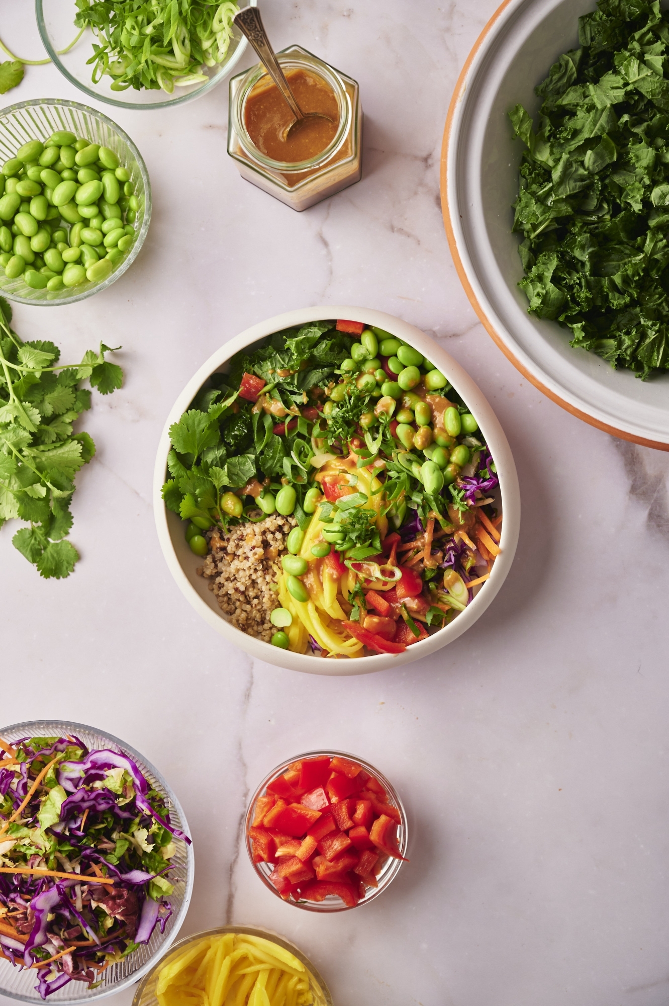 Thai quinoa bowls with kale, edamame, carrots, cabbage. green onions, and Thai peanut sauce in a bowl.