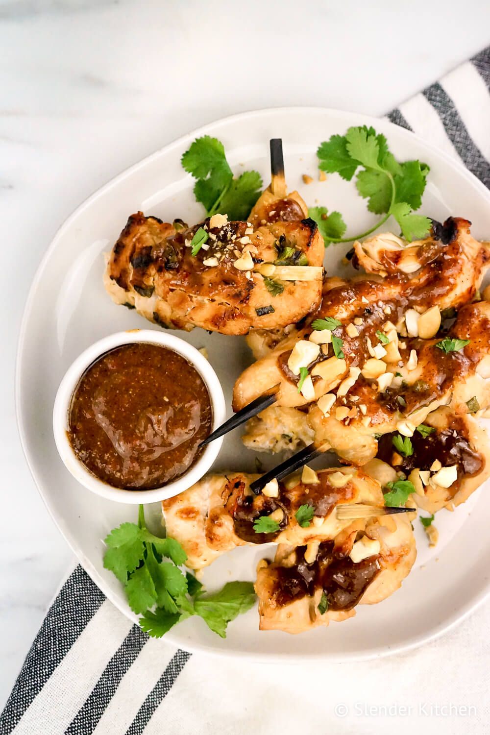 Thai Chicken Skewers with cilantro and crushed peanuts on a white plate with a blue linen napkin.