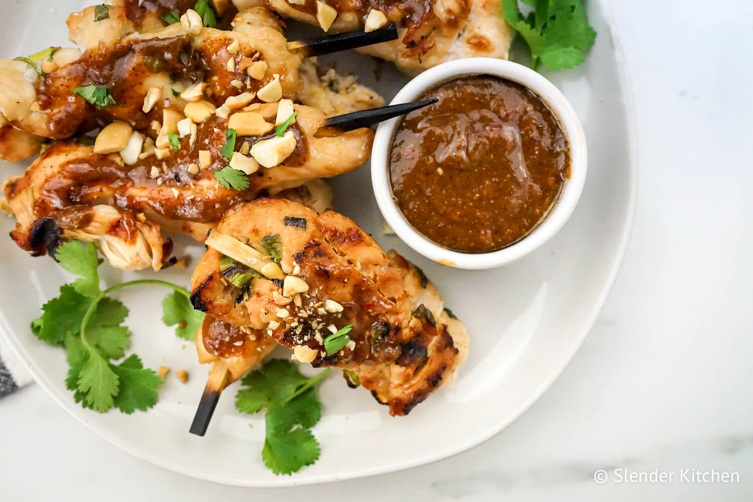 Thai Chicken Skewers close up with cilantro and peanut sauce and a white background.