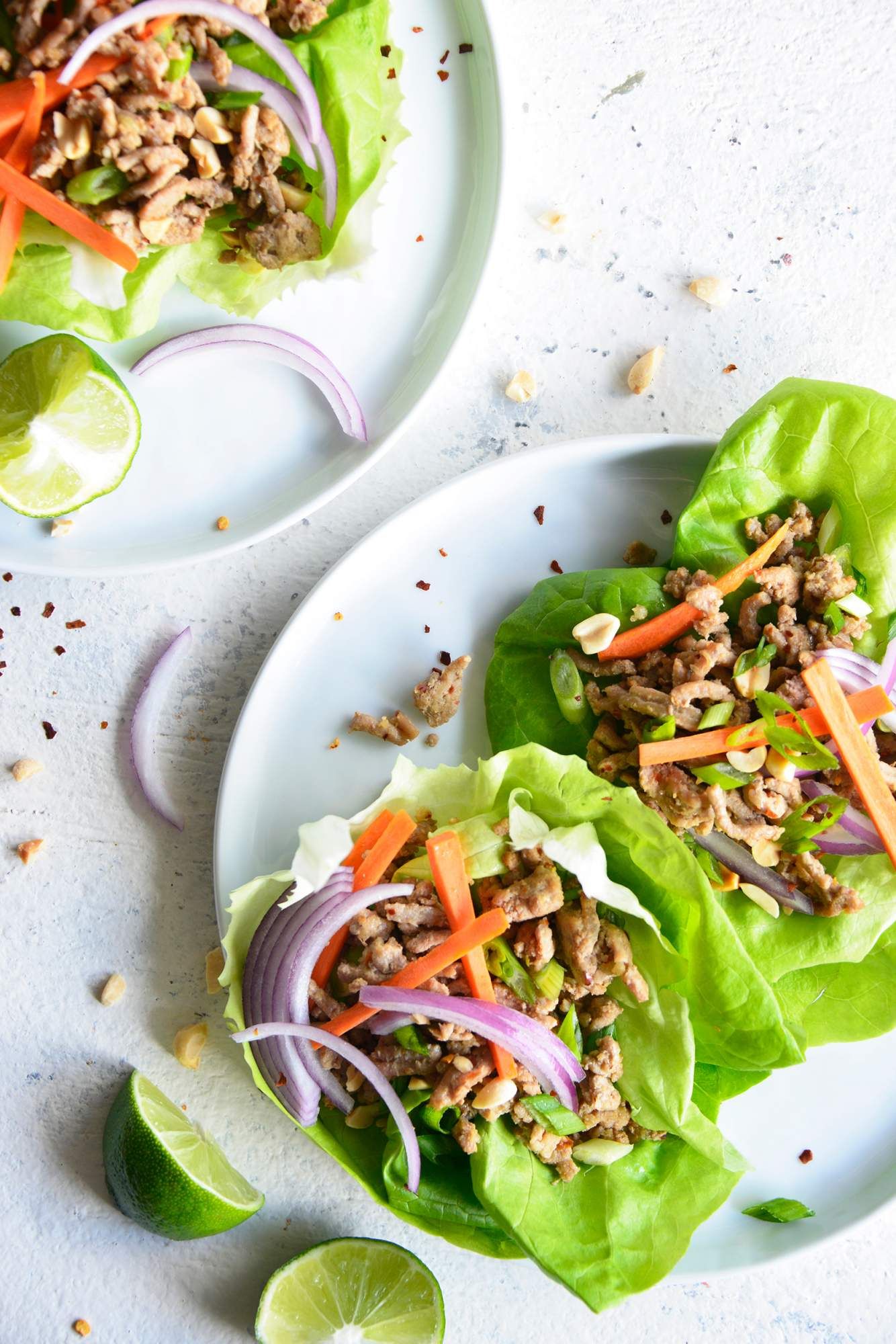 Lettuce wraps with ground turkey, Thai sauce, red onions, cilantro, carrots, and butter lettuce on a plate with limes.