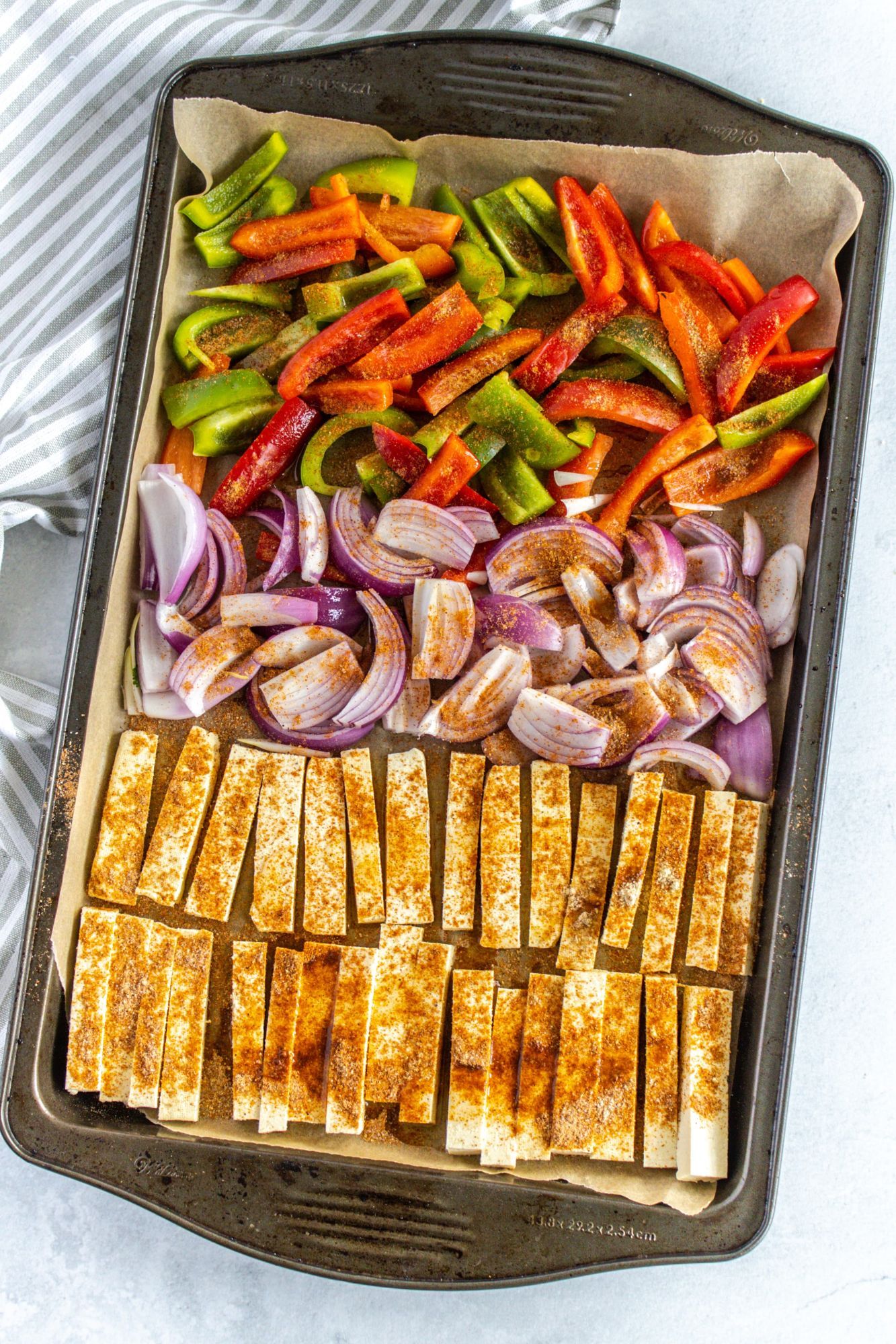 Sheet pan tofu fajitas with bell peppers, red onion, and fajita seasoning with tortillas and cilantro on the side.