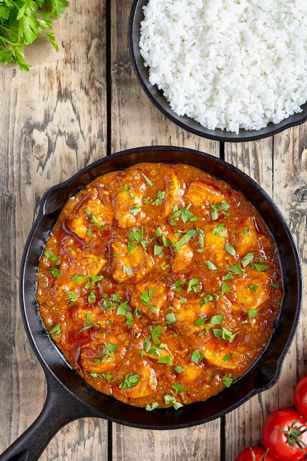 Tomato chicken thighs in a tomato sauce with cooked white rice and parsley.