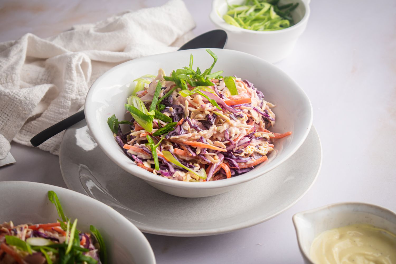 Three color coleslaw with shredded carrots and cabbage in a white bowl topped with green onions.