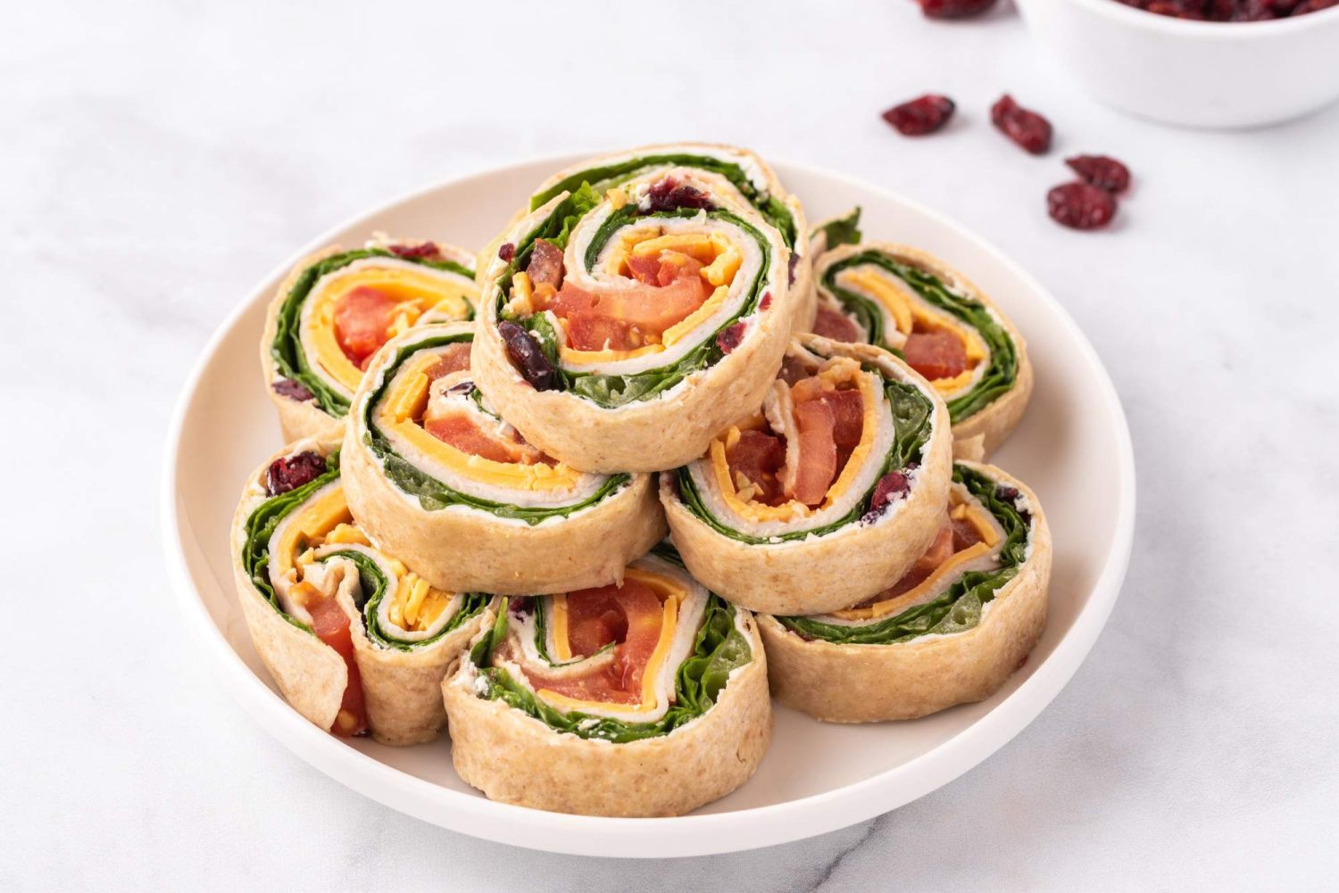 Turkey and cream cheese pinwheels with tomatoes, lettuce, cheddar cheese, and dried cranberries.