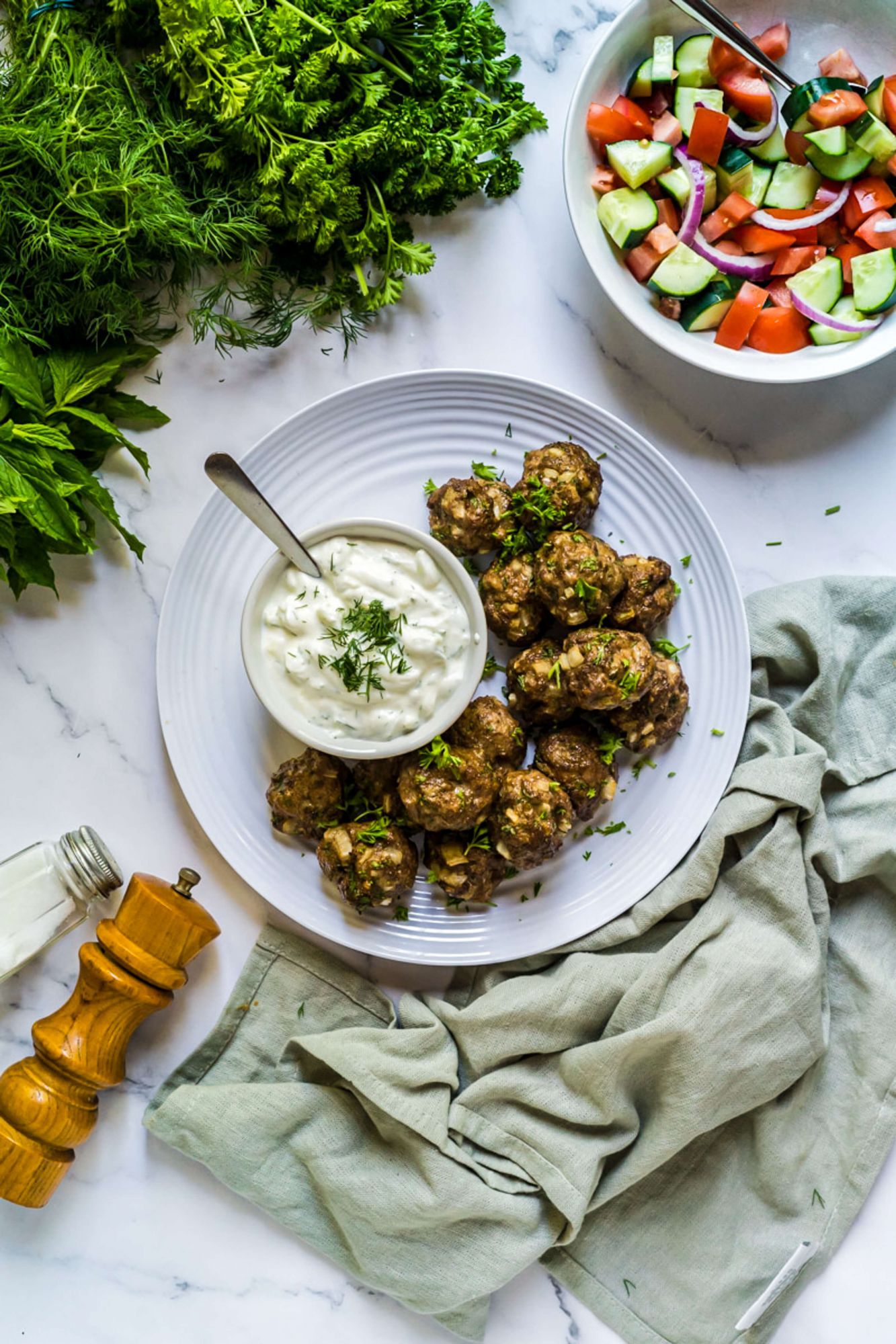 Lamb Turkish meatballs on a plate with yogurt dip and tomato, cucumber salad on the side.