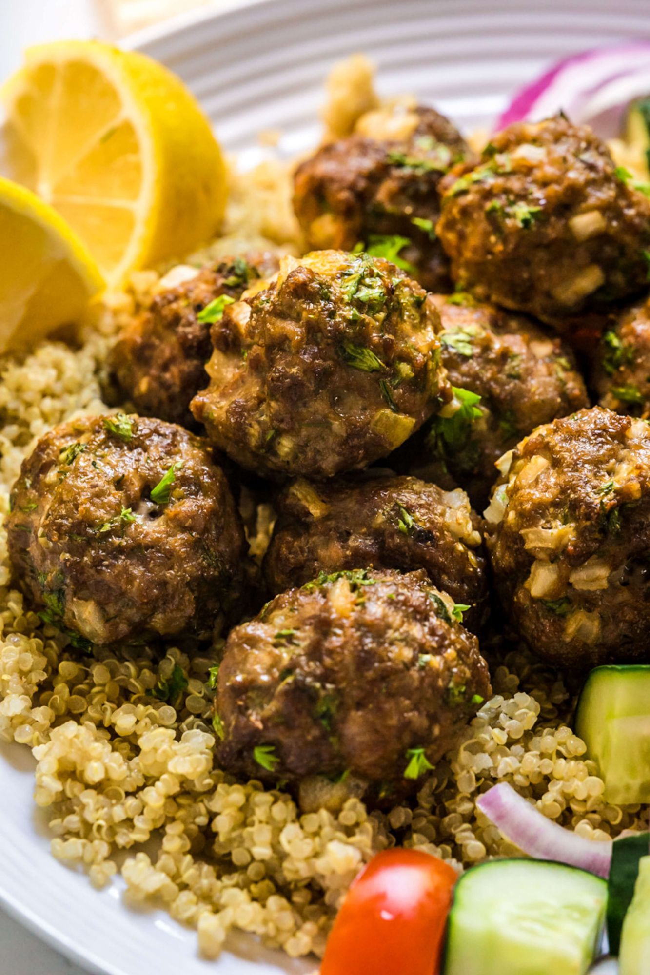 Lamb and ground beef Turkish kofte meatballs on a plate with quinoa, red onions, tomatoes, cucumbers, and lemon.