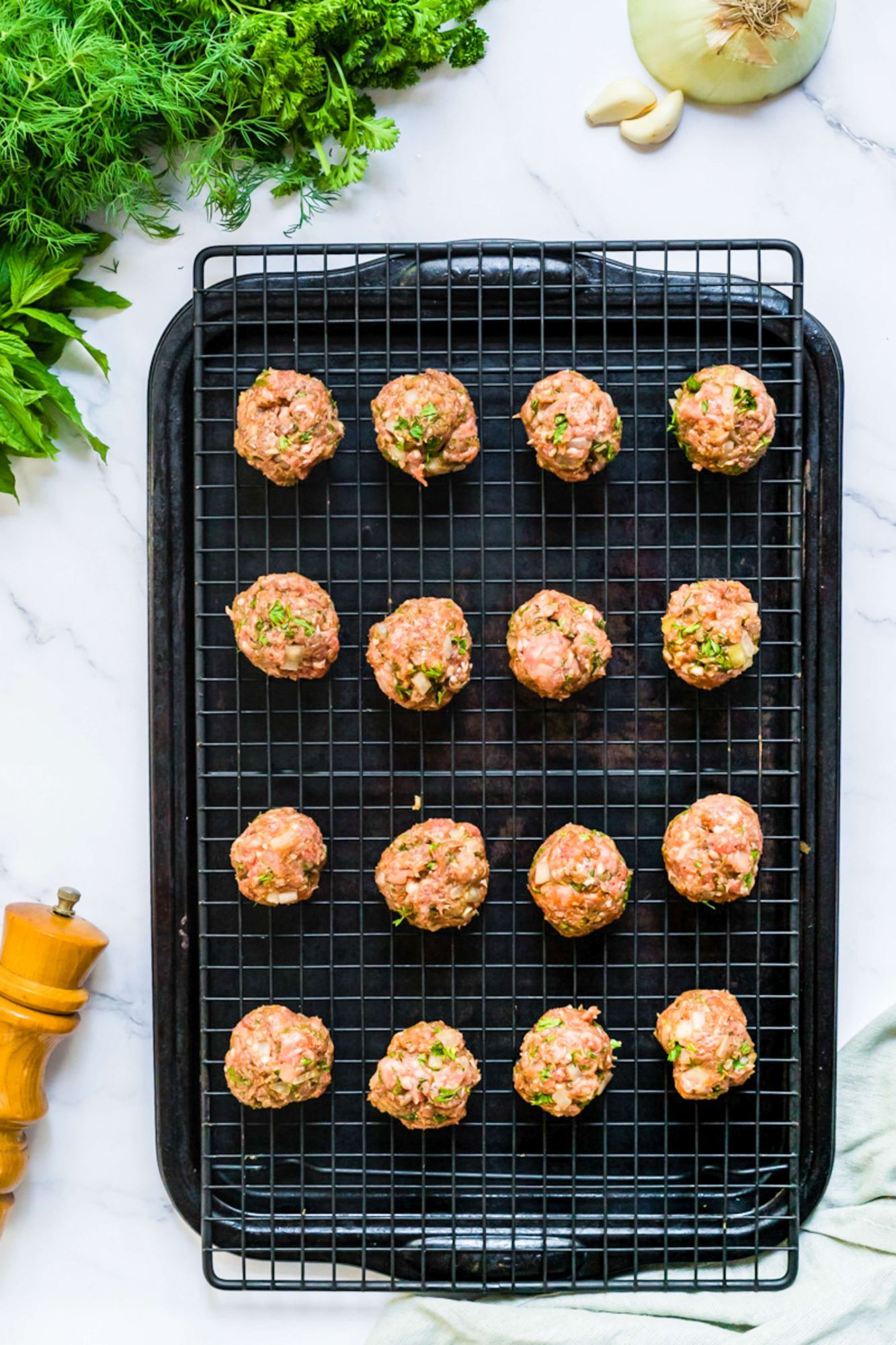 Kofte Turkish meatballs on a wire rack with onions, garlic, and fresh herbs before being cooked..