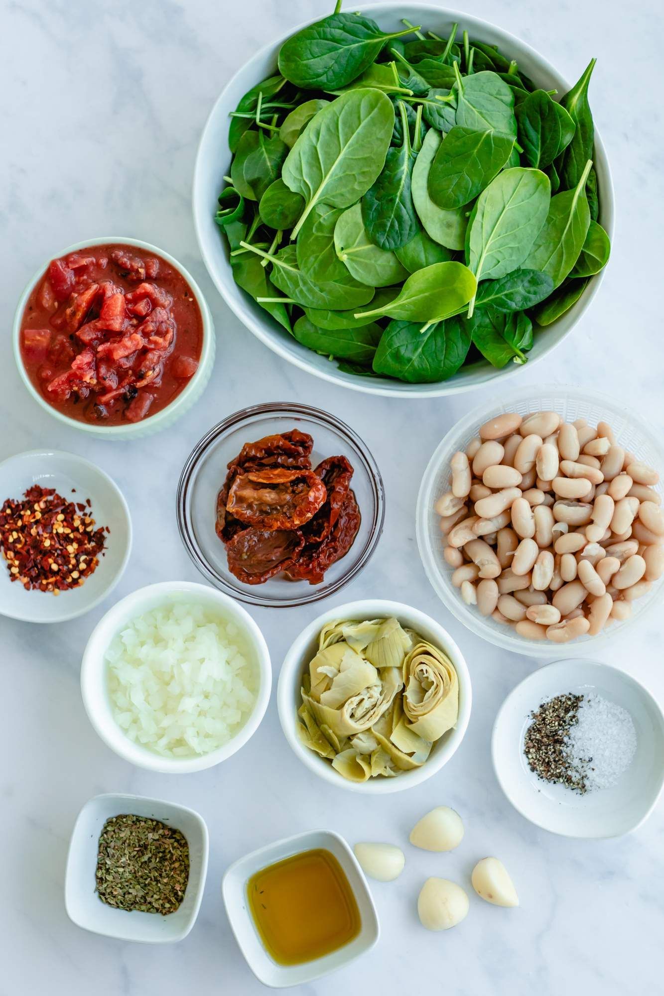 Ingredients for a Tuscan white bean skillet with cannellini beans, tomatoes, garlic, onion, spinach, and artichoke hearts.