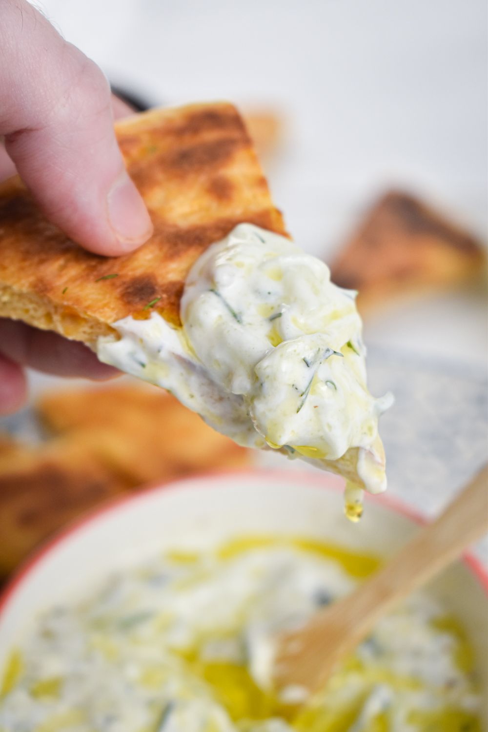 Greek tzatziki made with yogurt, cucumbers, garlic, and lemon in a bowl being scooped up with a pita bread.