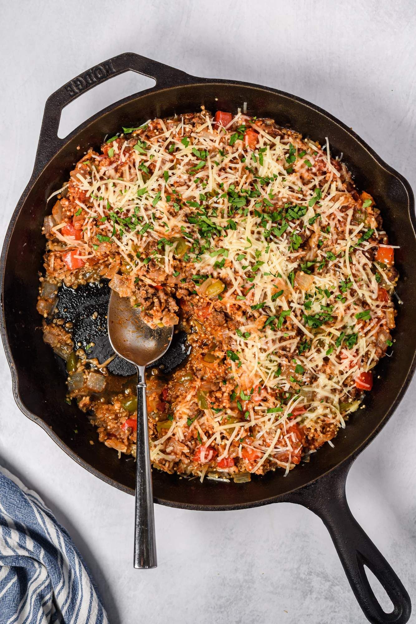 Stuffed peppers and ground beef with quinoa in a cast iron skillet with Parmesan cheese on top.