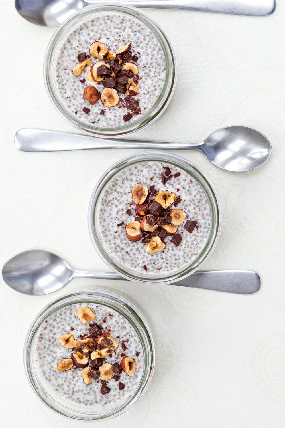 Vanilla chia seed pudding in three glass jars with three spoons on a white marble counter.