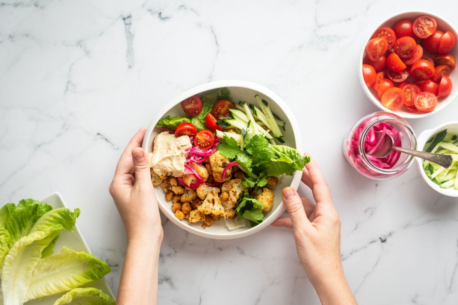 Cauliflower shawarma with chickpeas and vegetables in a white bowl being held by two hands.