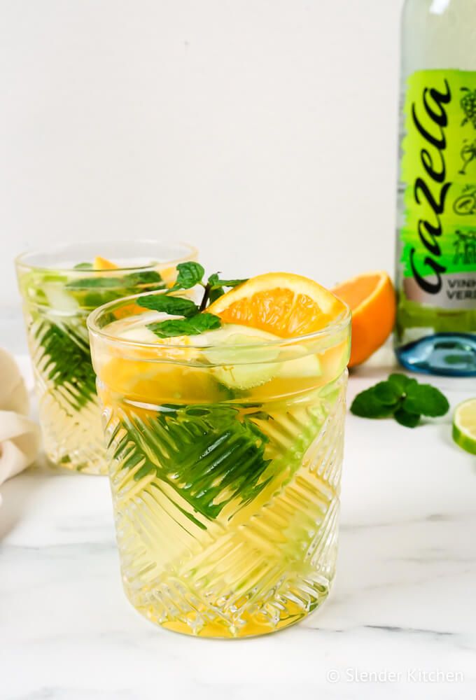 White sangria with vinho verde, green grapes, aples, lemon, lime, and orange in two glasses.