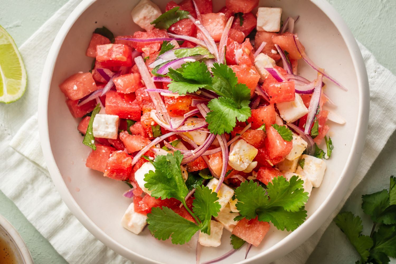 Fresh watermelon feta salad with sliced red onions, fresh cilantro, and lime vinaigrette in a white bowl.