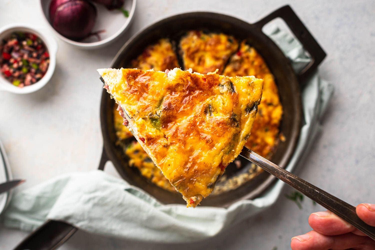 Piece of a western frittata on a serving fork with eggs, peppers, onions, and ham cooked in a skillet.