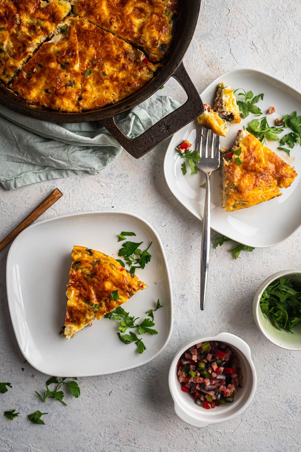 Western frittata made with eggs, bell peppers, red onion, and ham  served on two plates with a fork.