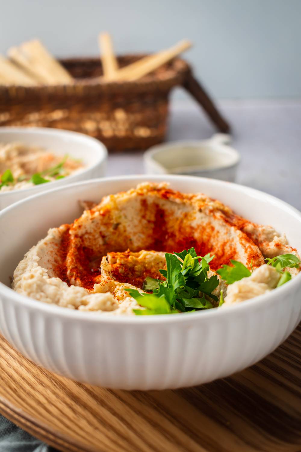 Hummus with white beans in two bowls served with paprika, olive oil, and herbs with breadsticks on the side.