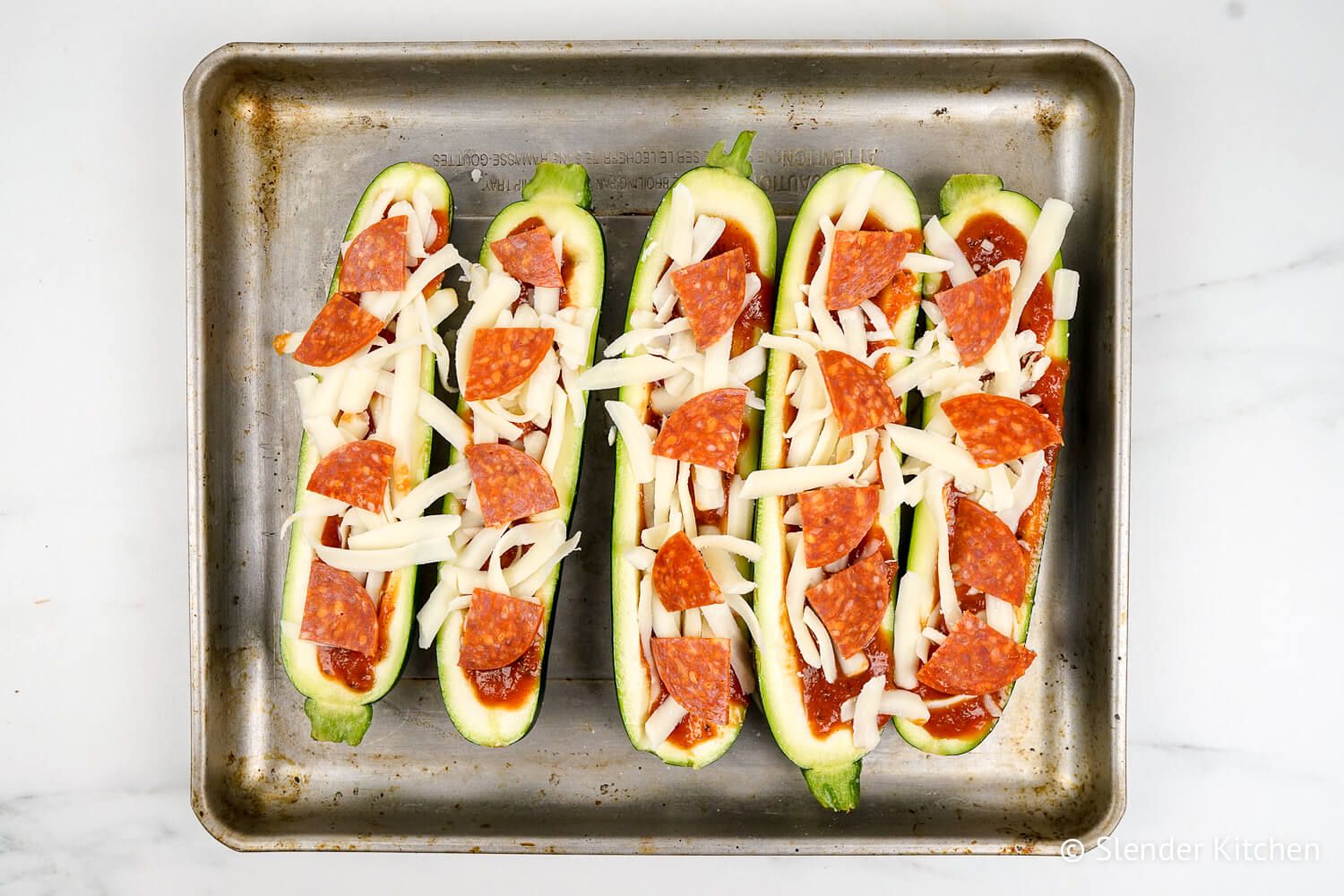 Zucchini pizza boats on a baking sheet before being cooked.