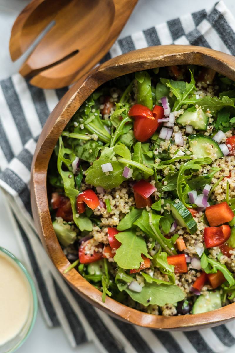 Mediterranean quinoa bowls with cooked quinoa, arugula, red peppers, cherry tomatoes, red onions, olives, and hummus dressing. 