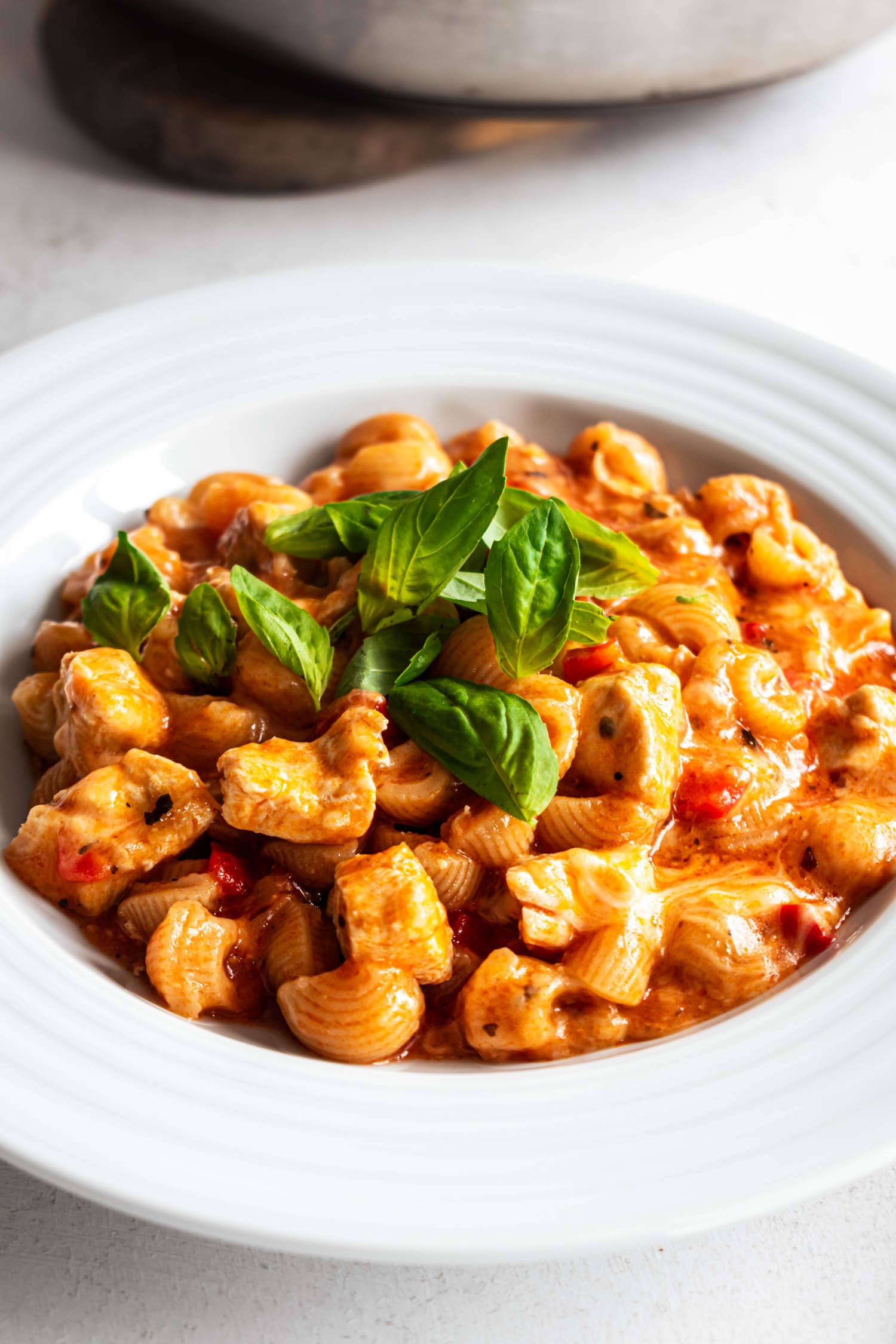 Bowl of chicken pasta with marinara sauce, chicken breast, red peppers, melted cheese, and fresh basil.