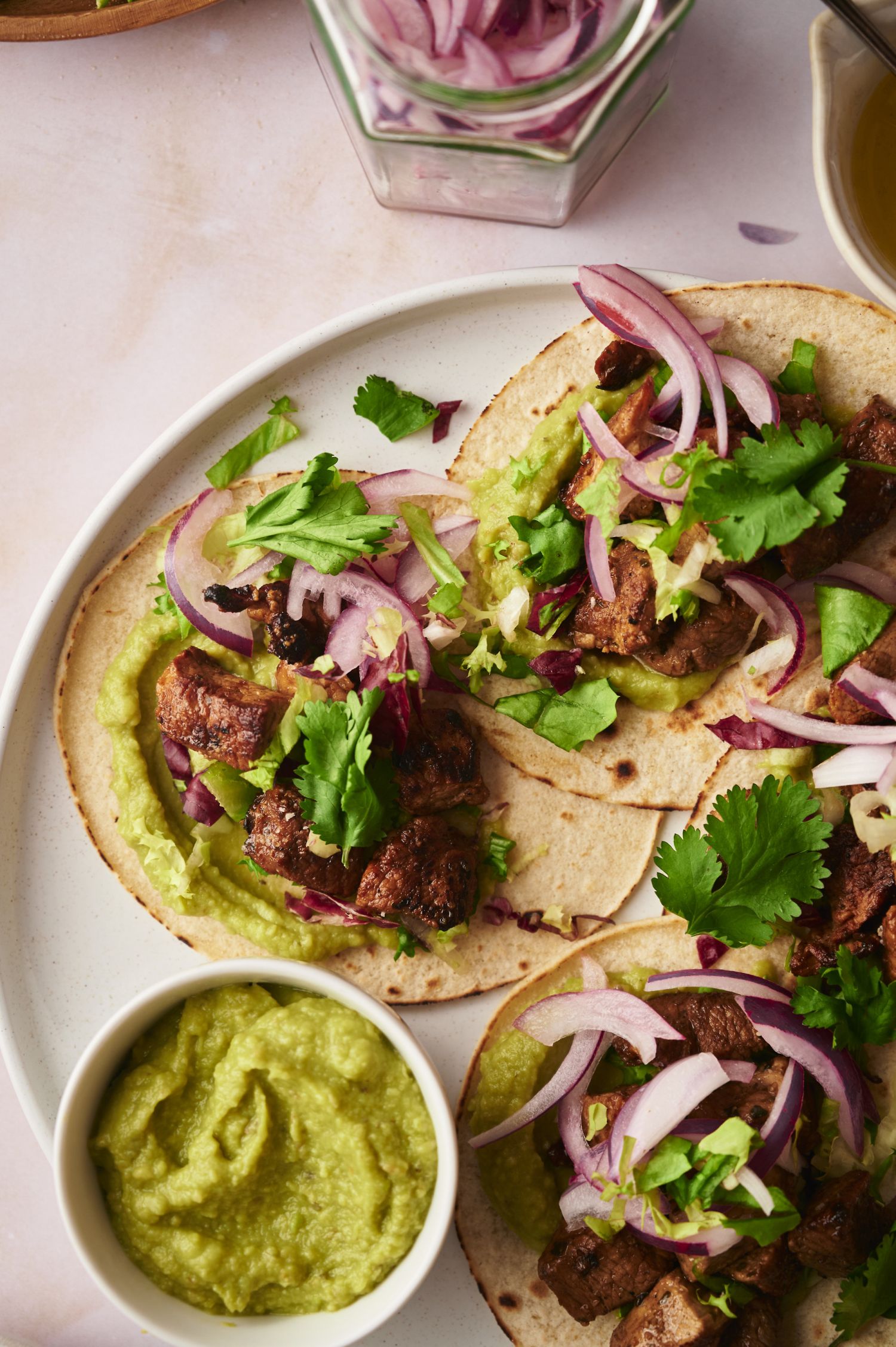 Tacos with crispy pork, red onions, cilantro, and avocado spread on corn tortillas.